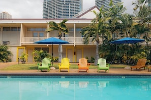 Un hotel con piscina, múltiples sillas Adirondack de colores y palmeras.