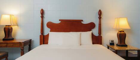 A hotel room with a large bed, wooden headboard, two bedside tables with lamps, and a nightstand with a clock.