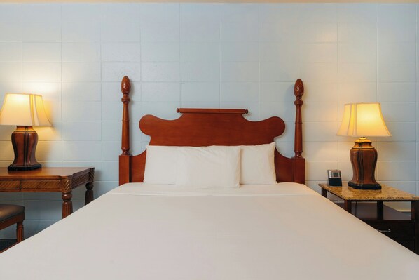 A hotel room with a large bed, wooden headboard, two bedside tables with lamps, and a nightstand with a clock.
