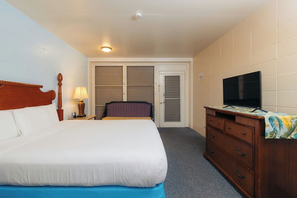 Une chambre d’hôtel avec un lit, un téléviseur posé sur une commode en bois, une porte avec un moustiquaire et une lampe fixée au mur.