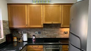 Una cocina compacta con armarios de madera, un refrigerador de acero inoxidable, horno integrado y lavadora.