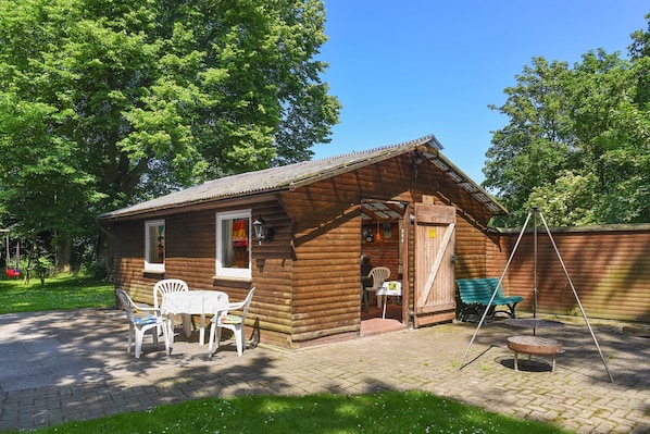 A wooden cabin with a brick patio, a small table with chairs, and a swing set.