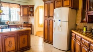 Une cuisine avec des meubles en bois, un réfrigérateur blanc et un sol carrelé.