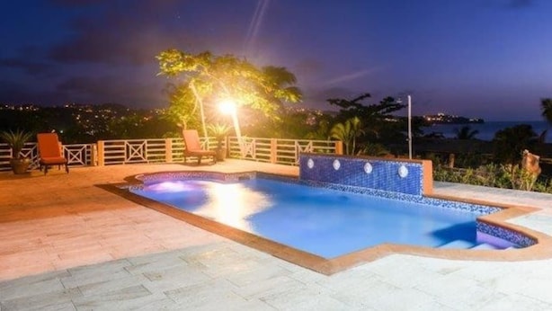 Une piscine dont le bord est recouvert de carrelage, entourée d’une terrasse avec des chaises et une clôture.