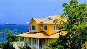 Un bâtiment jaune doté d’un balcon, qui donne sur une étendue d’eau et sur un navire visible au loin.