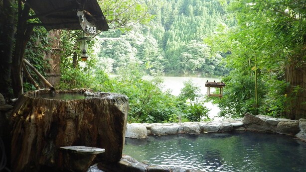A serene outdoor hot spring area with a wooden structure and a stone basin. - Kosenkaku Yoshinoya (Totsukawa)