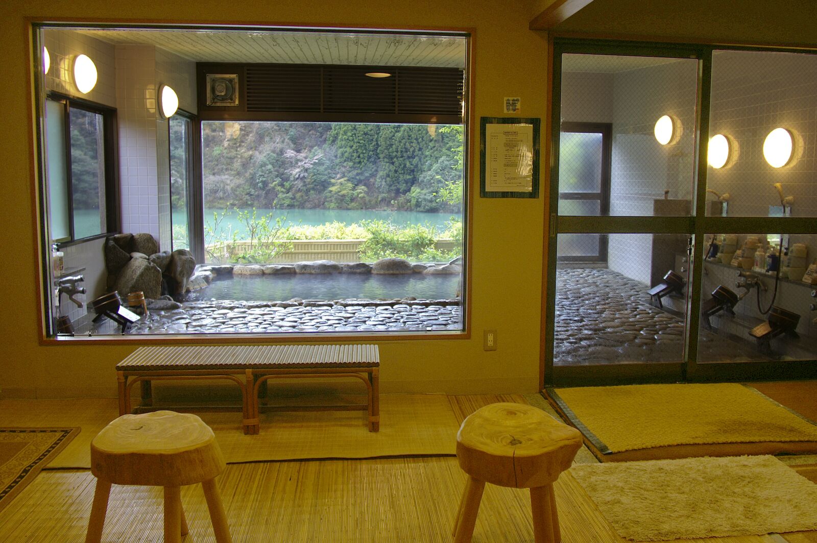 A room with a large window overlooking a pond, a wooden bench, and a small stool.