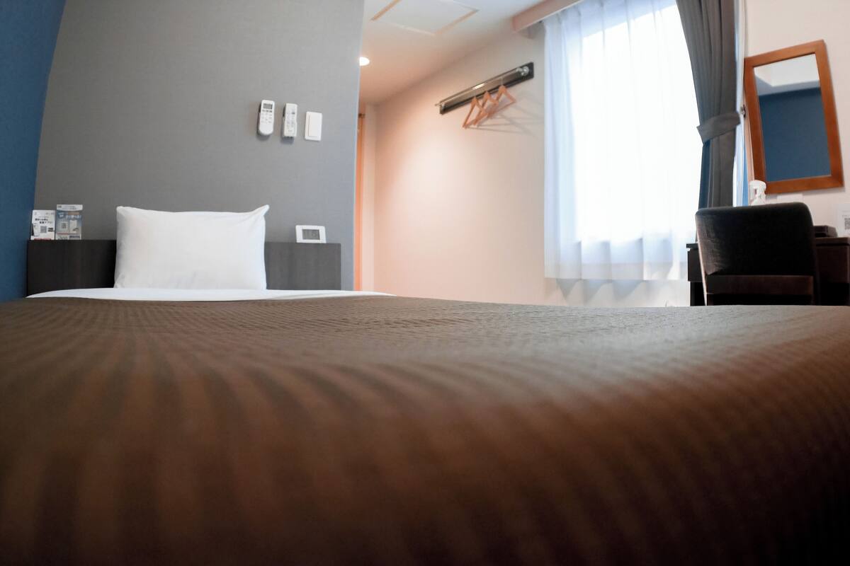 A hotel room with a large bed, a desk, a chair, a mirror, and a window with curtains.