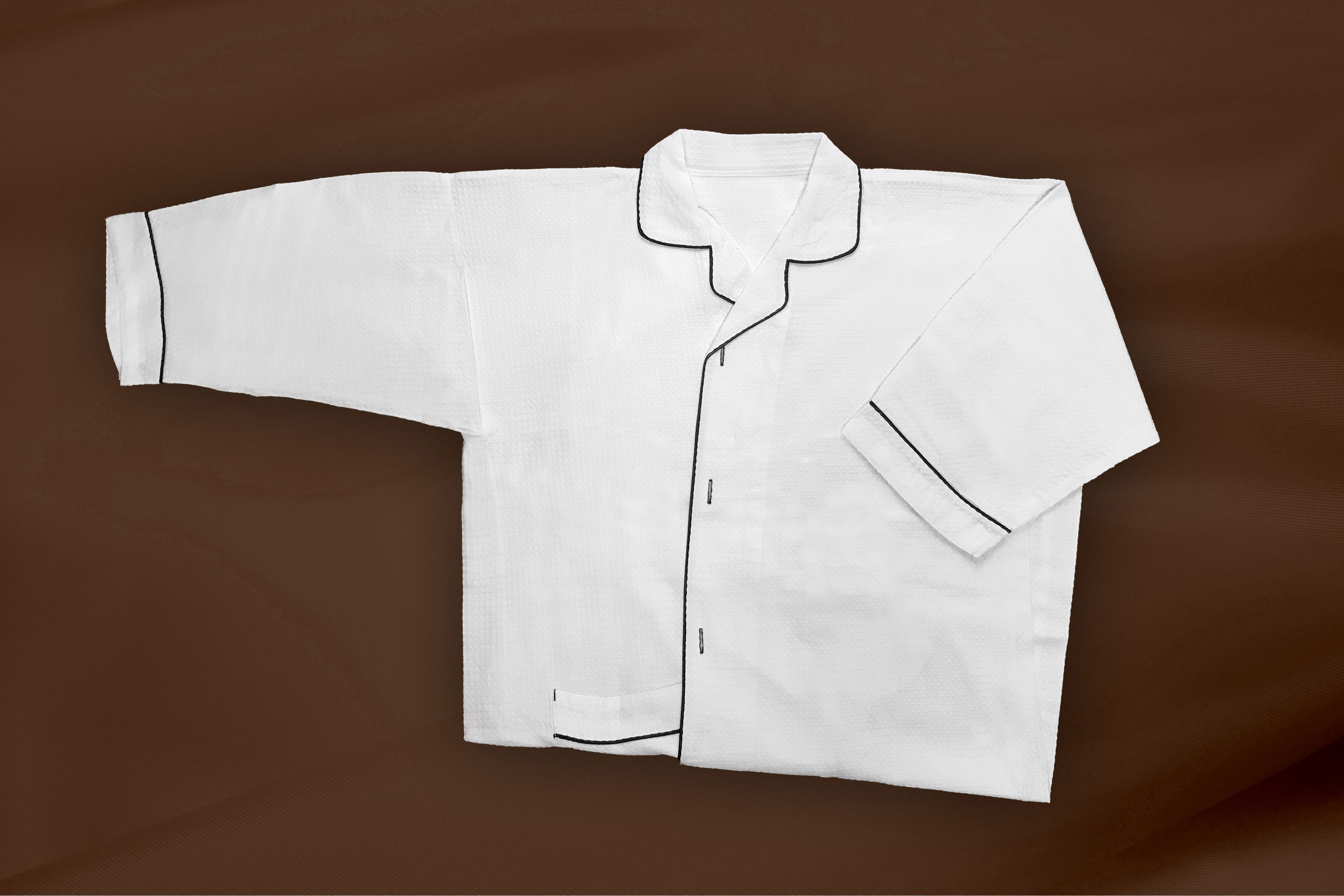 A white shirt with black piping on a brown background.