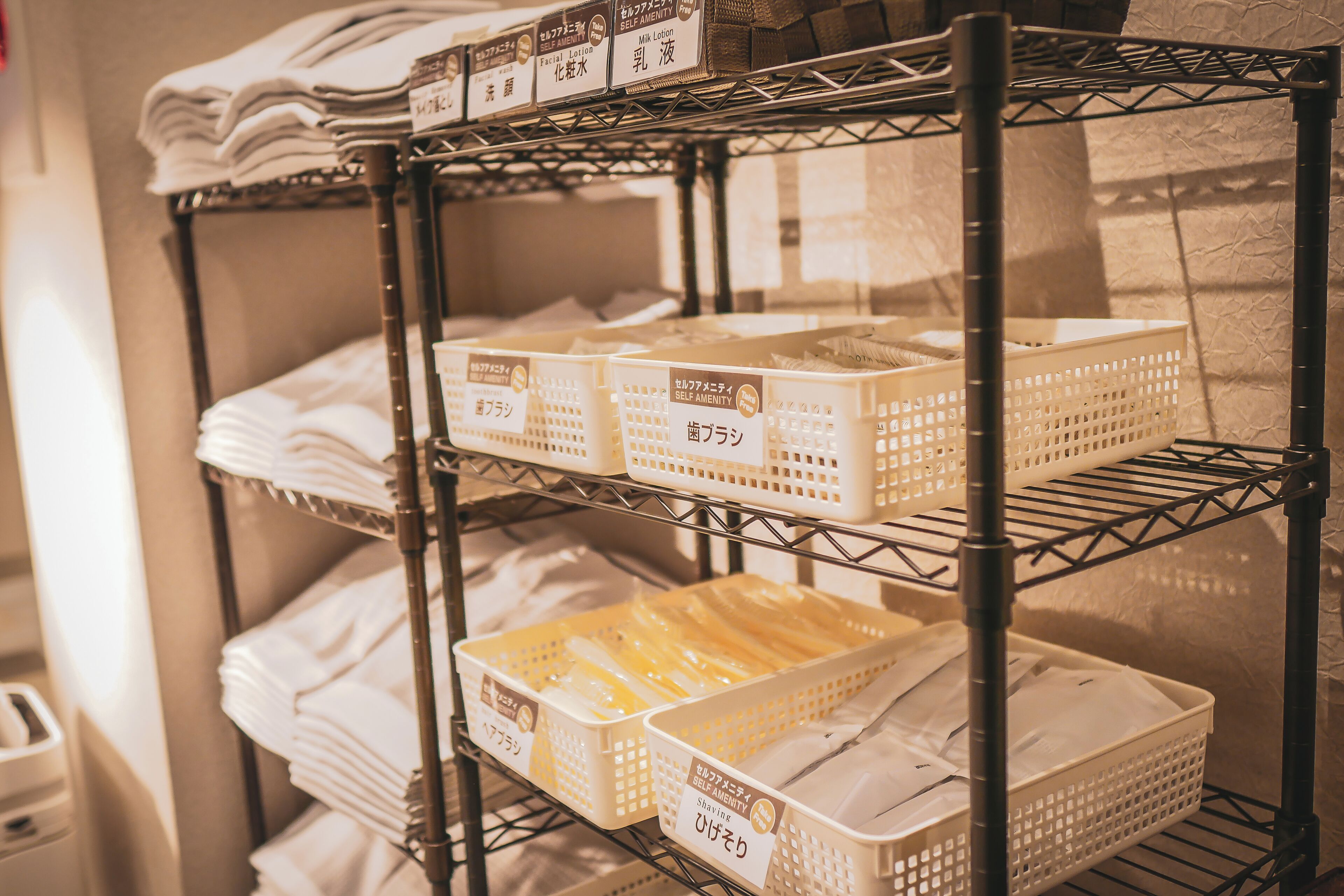 A shelf with neatly stacked white towels and baskets labeled with Japanese text.