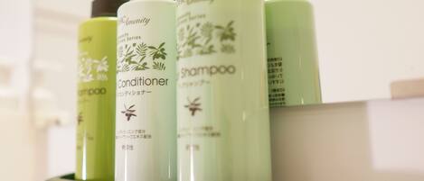 A set of green and white DHG Amenity shampoo and conditioner bottles on a shelf.