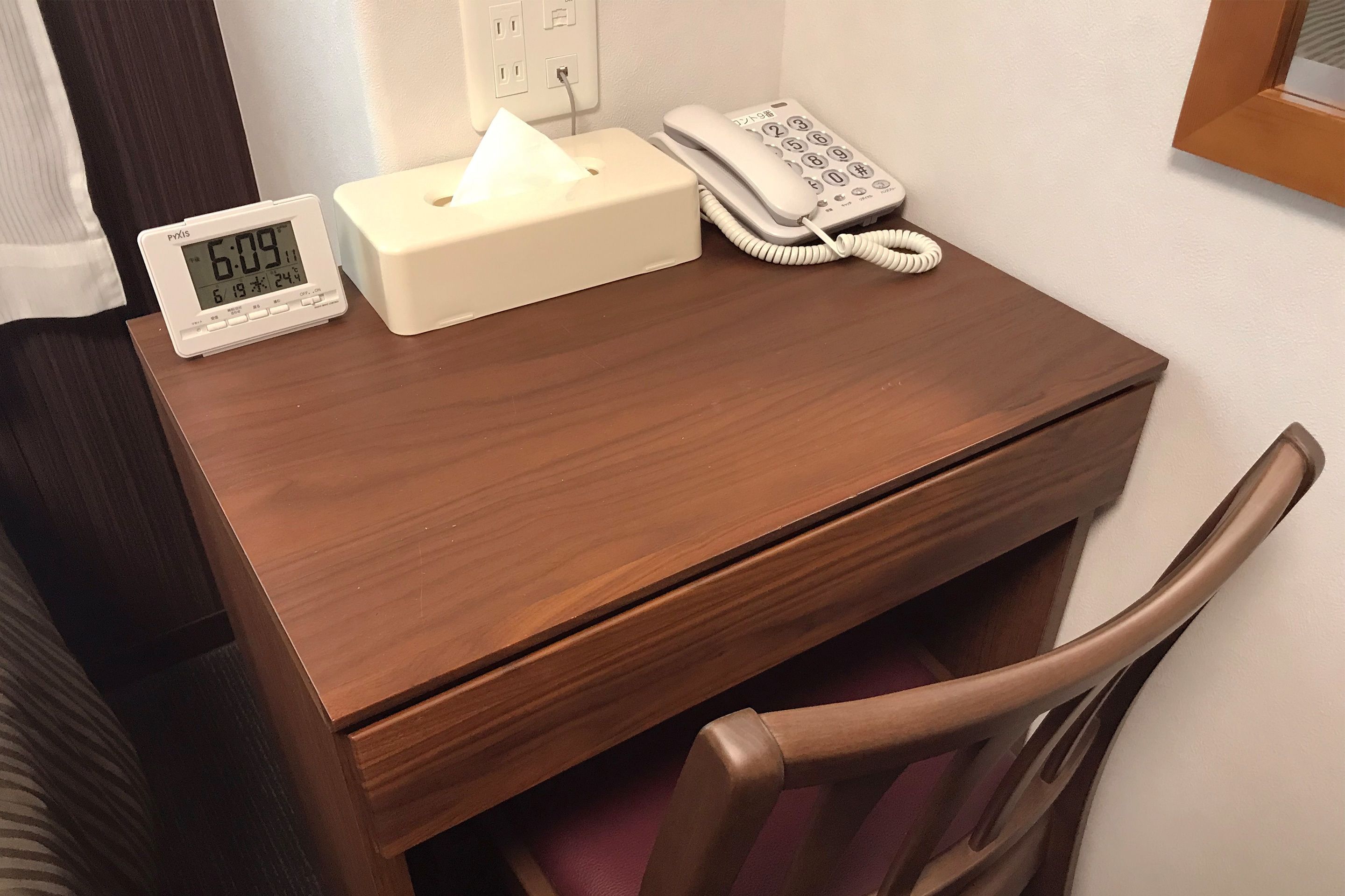 Un escritorio de madera con una caja de pañuelos, un reloj digital y un teléfono.