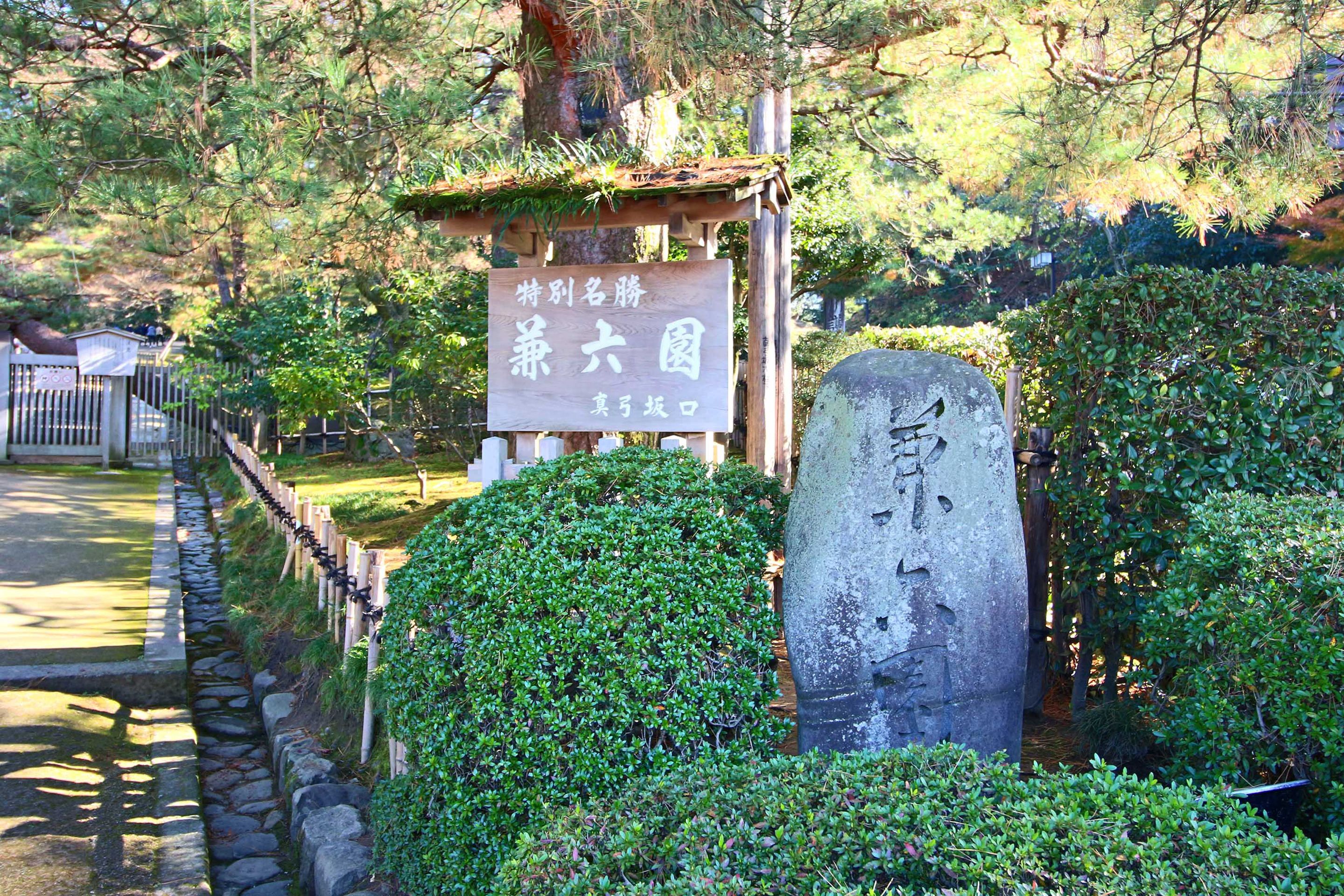 Ein Steins Denkmal mit japanischen Schriftzeichen, umgeben von üppigem Grün und einem Holzschild mit Text.