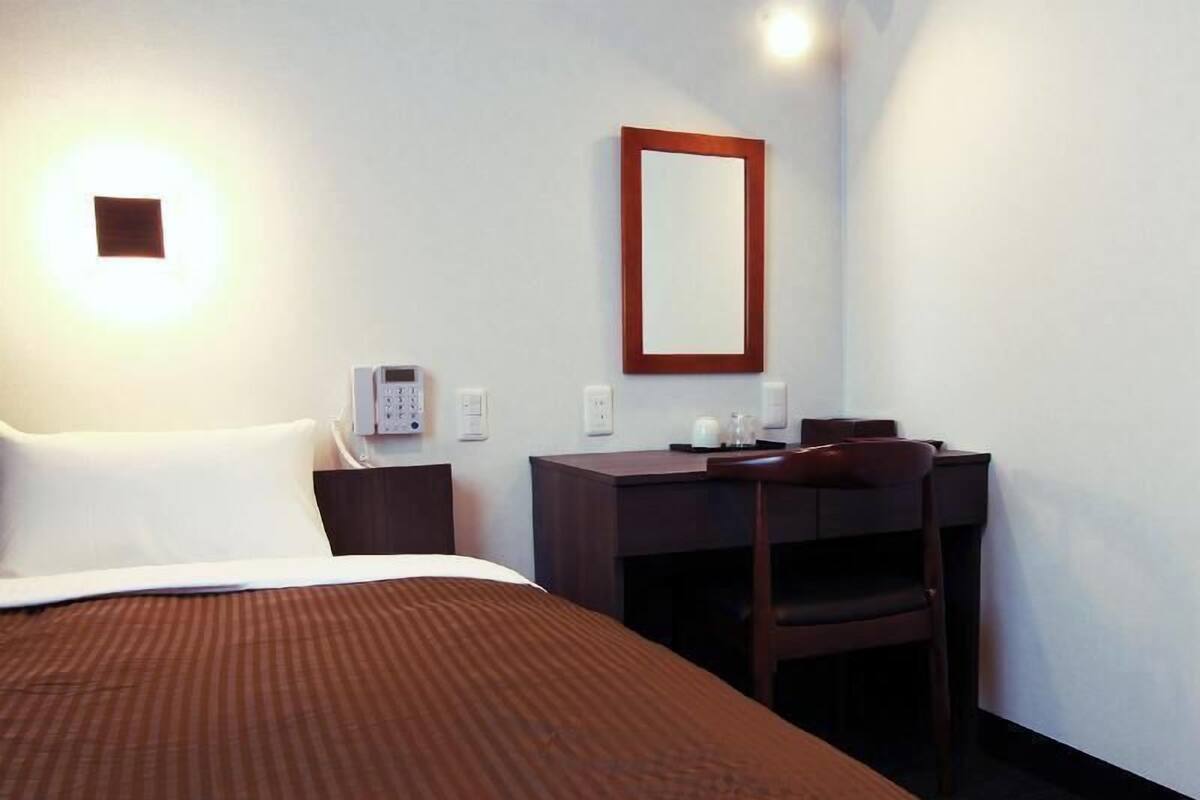 Habitación de hotel con cama, escritorio, silla, teléfono y espejo.