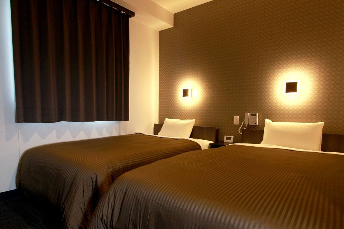 Une chambre d’hôtel avec deux lits, des rideaux foncés, un papier peint à motifs et des lampes de chevet.