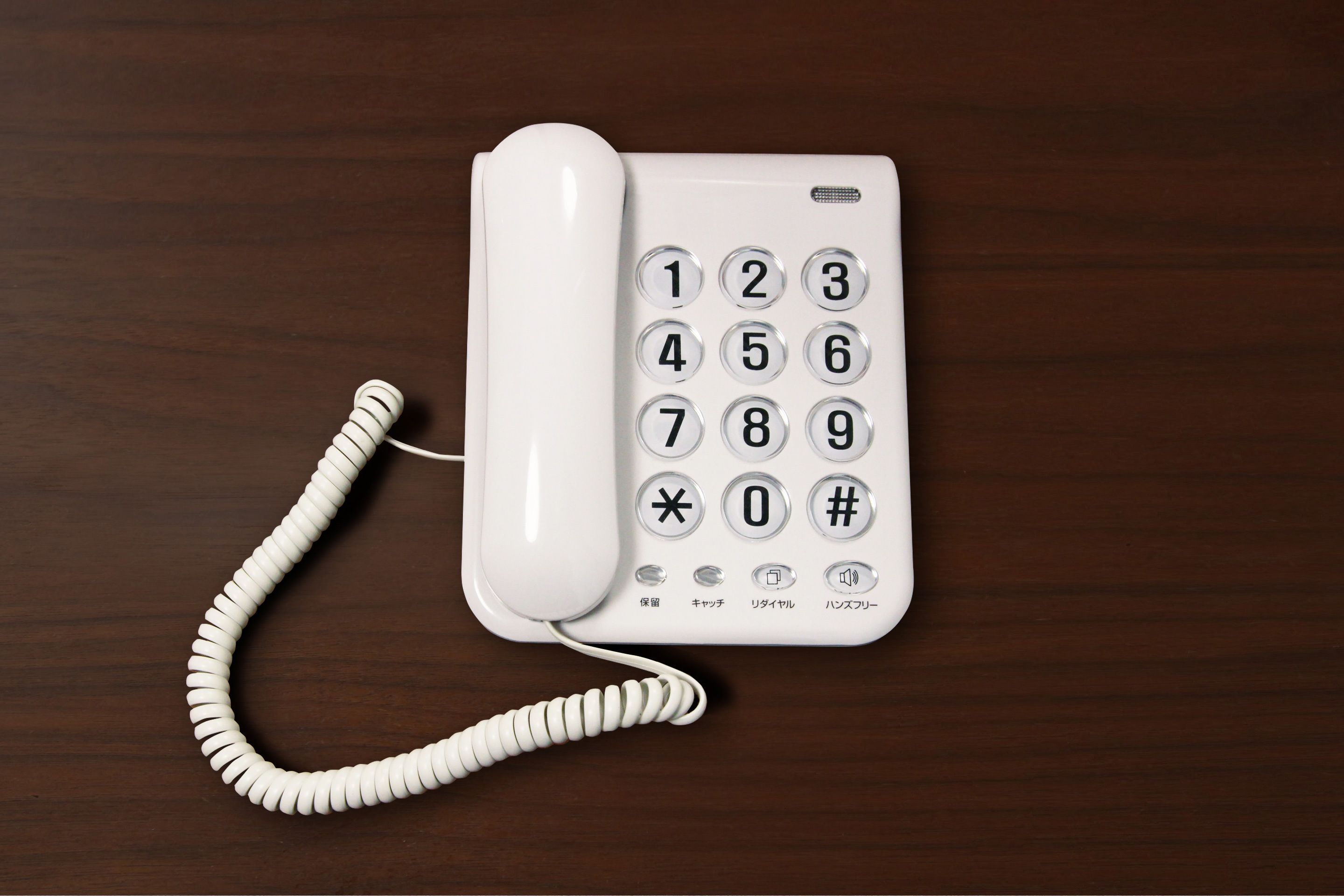 Un téléphone blanc avec un fil enroulé, posé sur une surface en bois.