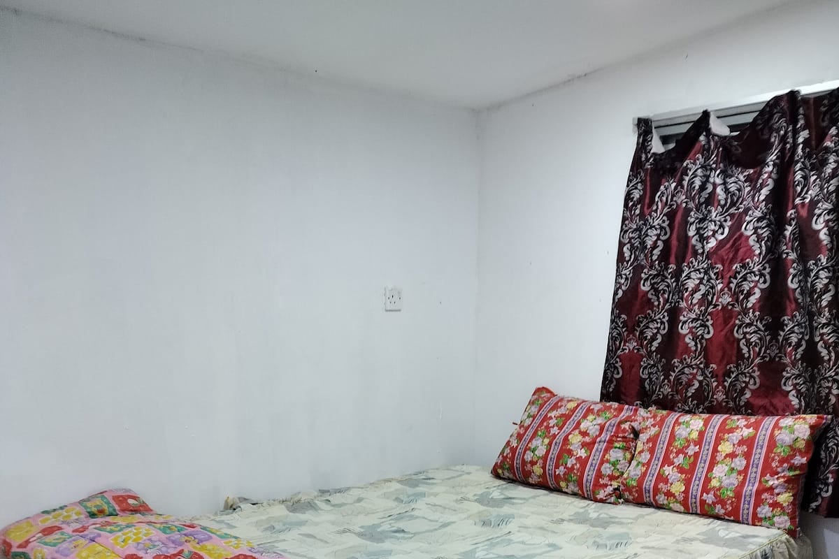 Un lit avec une couette aux couleurs vives et des bordures jaunes, un coussin à motifs et un rideau foncé.
