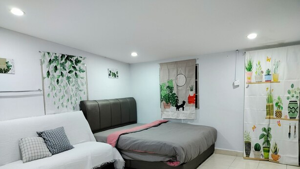 A modern bedroom with a grey sofa, a bed with a grey and pink bedspread, and a wall decorated with plant-themed curtains. - 223 Taman Malaysia (Alor Setar)