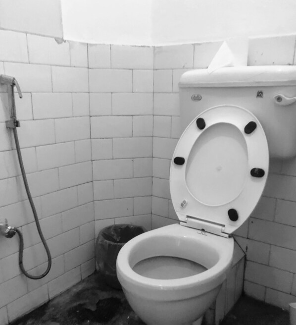 A white toilet with a raised seat and a bidet attachment in a tiled bathroom. - Himal Inn (Lalitpur)