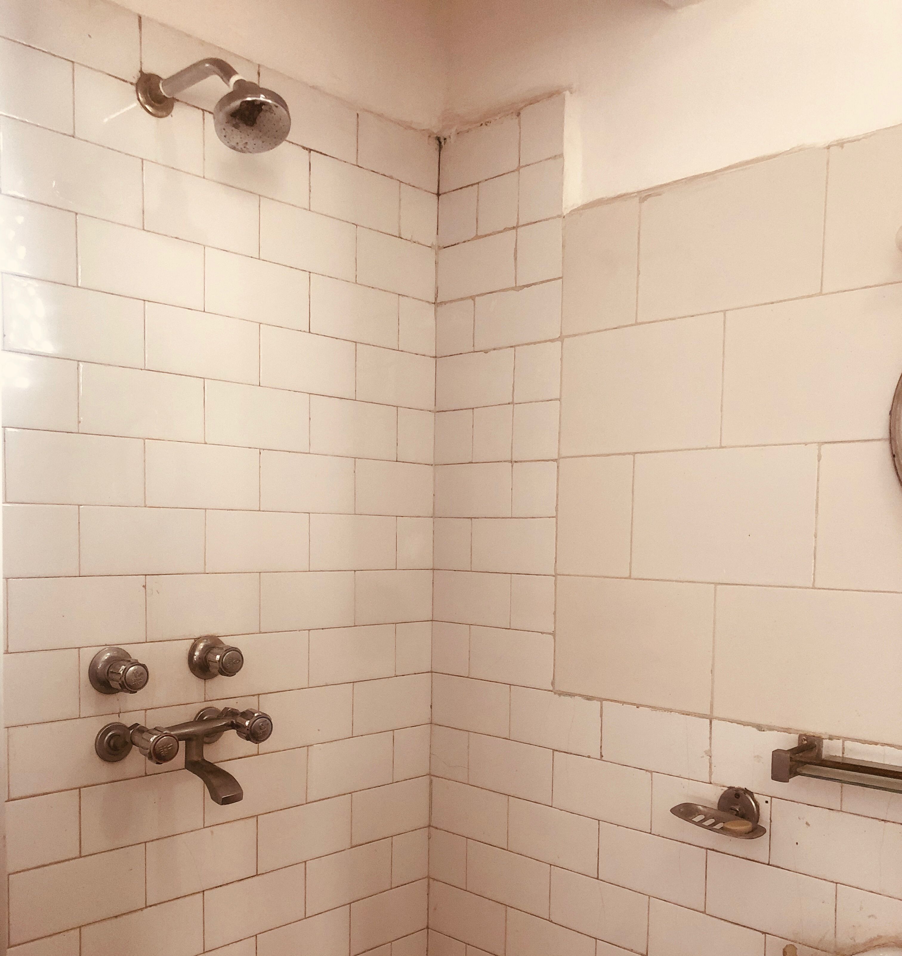 A corner of a bathroom with white tiled walls and a shower area.
