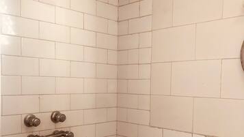 A corner of a bathroom with white tiled walls and a shower area.