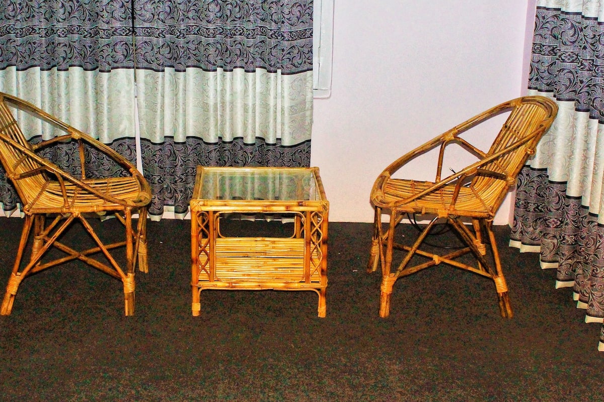 Two wicker chairs and a small table in a room with patterned curtains and a dark carpet.