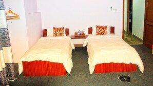 A hotel room with two single beds, a wooden nightstand, a small table with a tray, and a pair of slippers on the floor. - Himal Inn (Lalitpur)