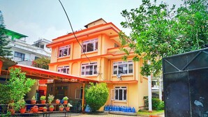 A multi-story building with a red roof and orange walls, featuring a covered outdoor seating area with potted plants. - Himal Inn (Lalitpur)