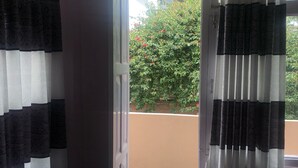 A room with a door leading to a balcony. The balcony has a view of a green bush with red flowers. - Himal Inn (Lalitpur)