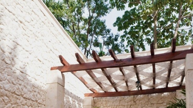 A person sitting by a pool with a pergola overhead, surrounded by stone walls and potted plants. - Casa Tavera (Mérida)