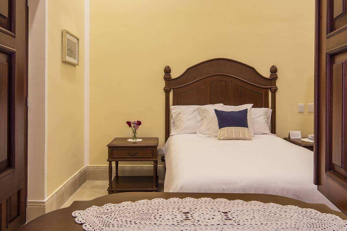 A bedroom with a wooden bed, a nightstand, a bedside table, and a ceiling fan.