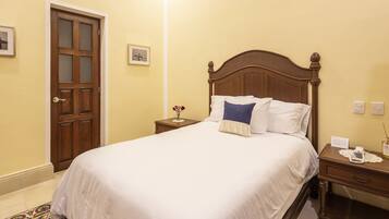 A neatly made bed in a room with a wooden ceiling, a patterned rug, and a door with glass panels.