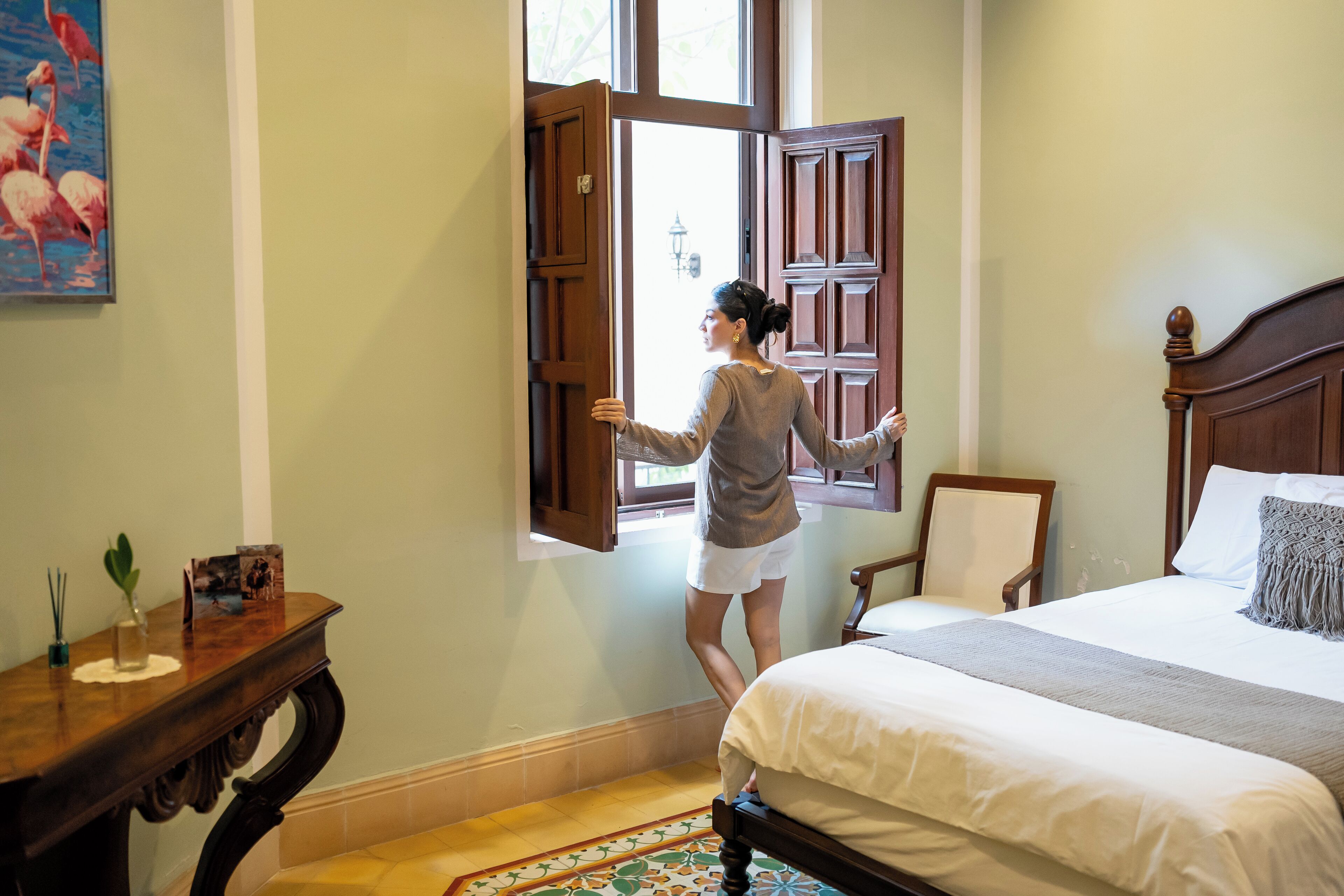 A bedroom with a bed, a nightstand, a wooden chair, and a window with open shutters.