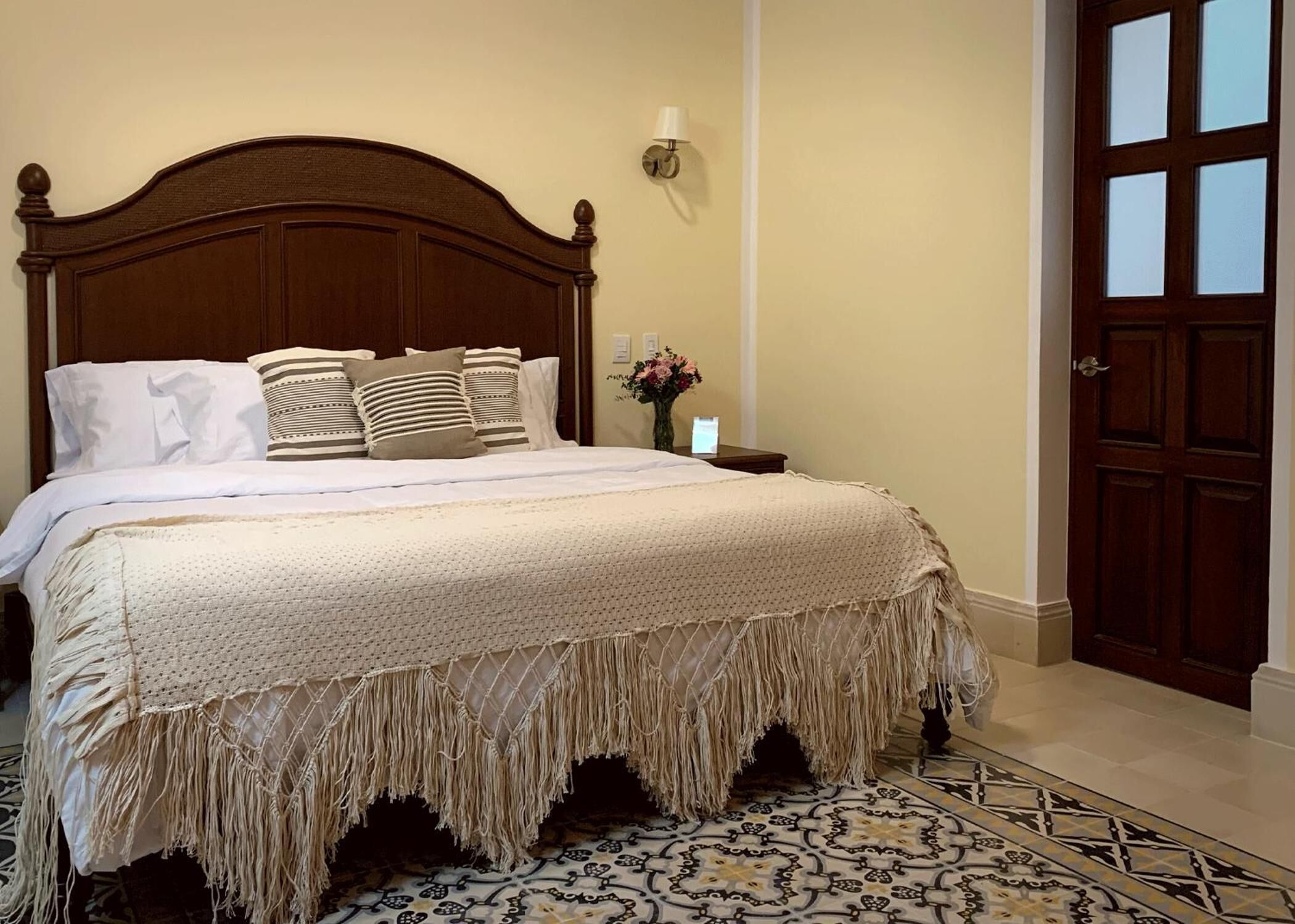 A neatly made bed with a wooden headboard, a decorative throw blanket, and a patterned rug.