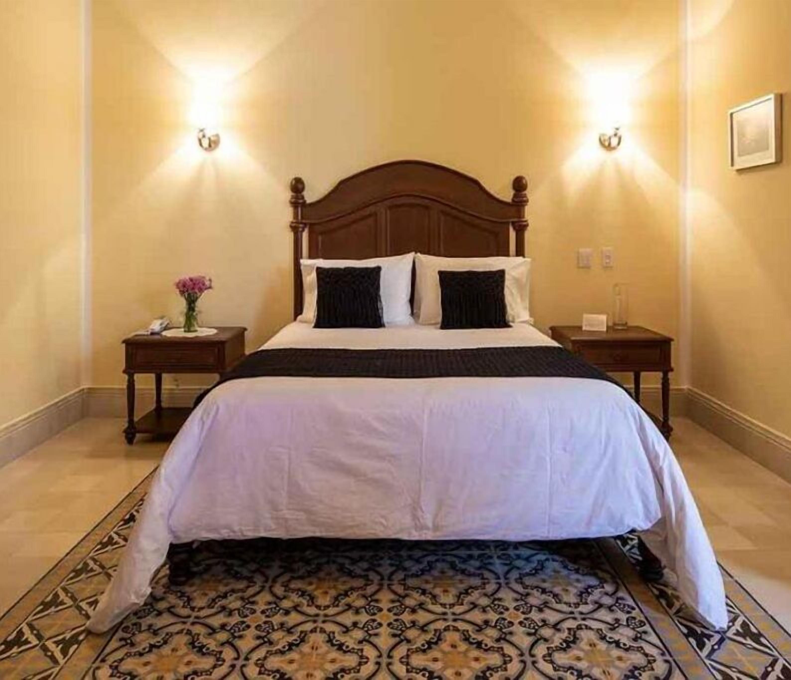 A neatly made bed with a wooden headboard, two bedside tables, and a patterned rug.
