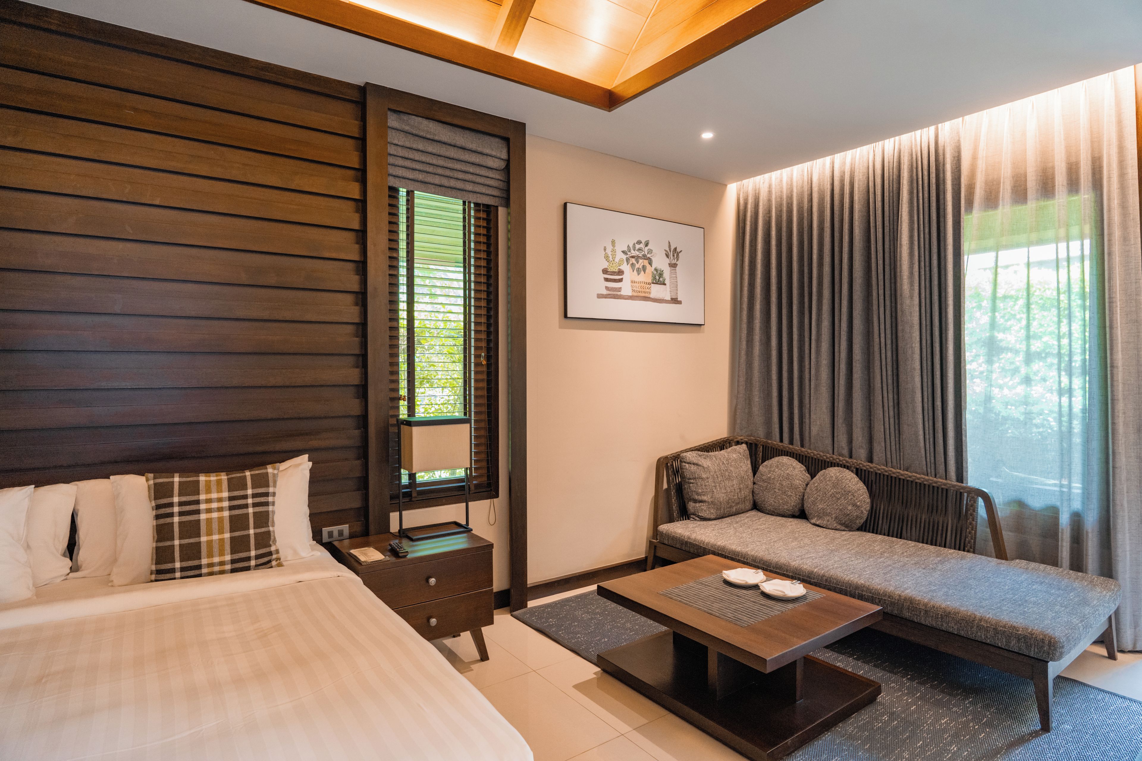 Une chambre d’hôtel moderne avec un grand lit, un canapé, une petite table et une fenêtre avec des rideaux.
