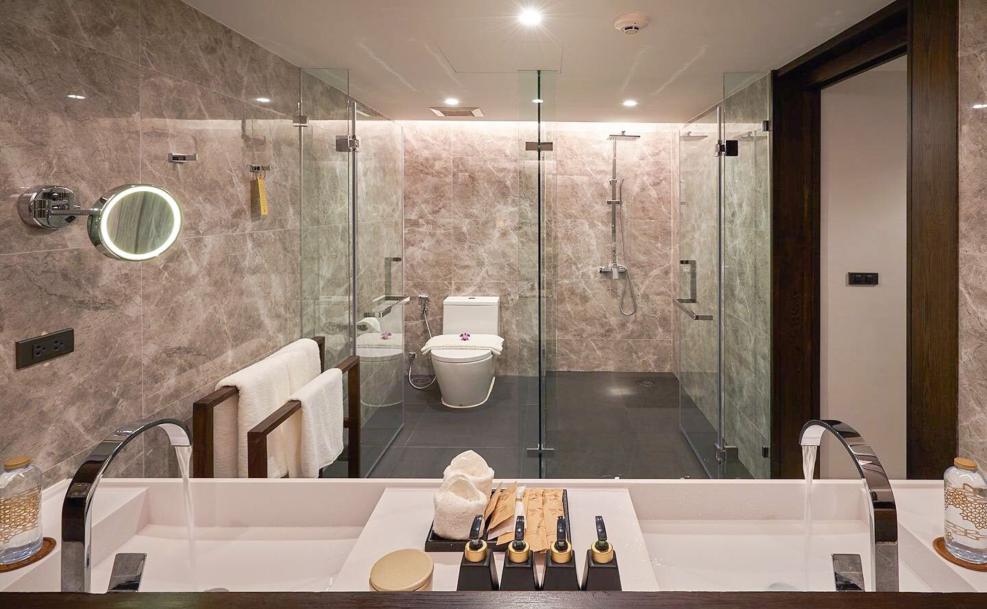 A modern bathroom with a glass-enclosed shower, a large mirror, and a vanity with toiletries.