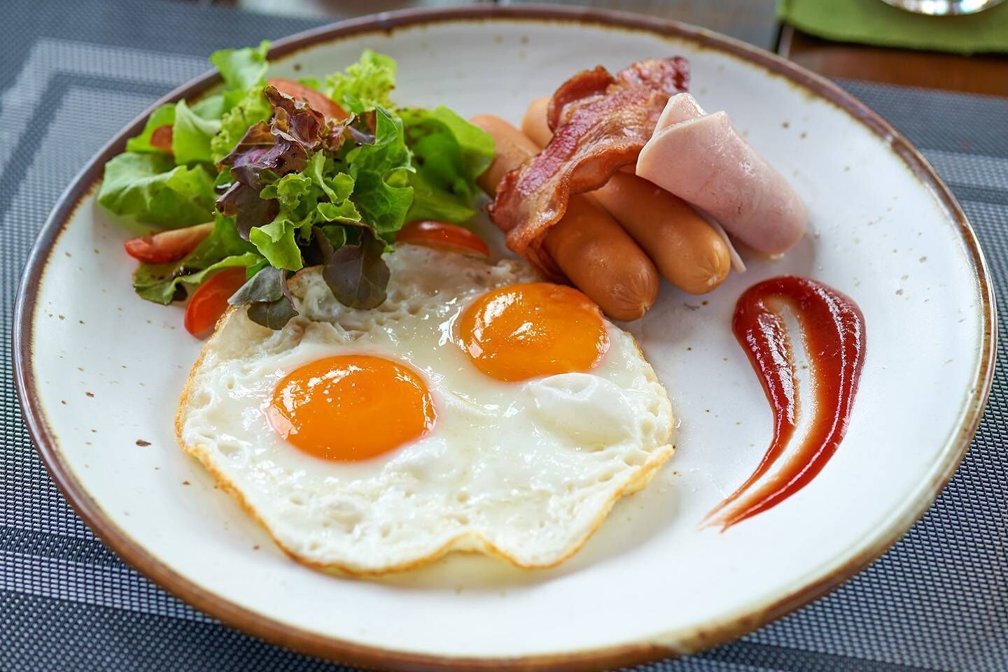 A plate with two sunny-side-up eggs, bacon, sausages, and a side salad.
