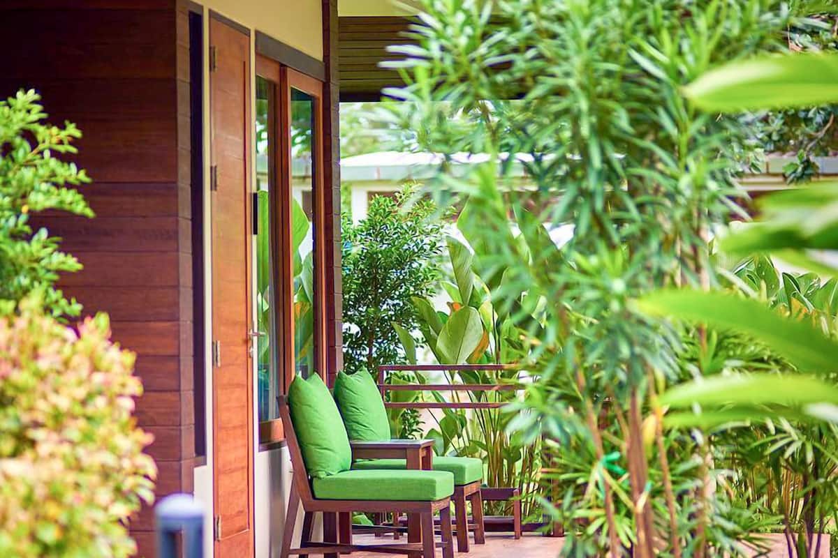 A wooden building with a covered porch, green chairs, and a pathway leading to the entrance.