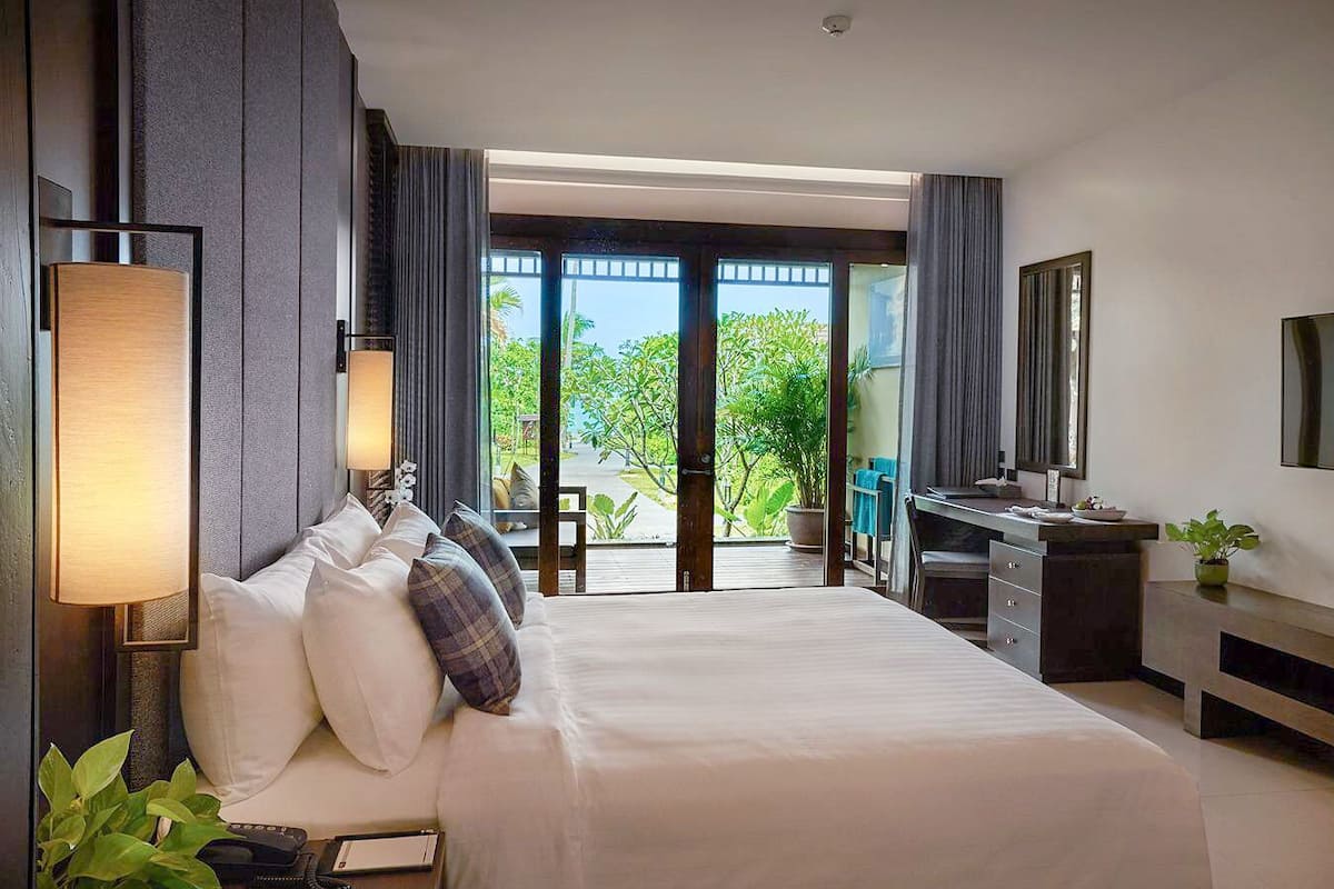 A hotel room with a large bed, a desk, a TV, and a view of the outdoors.