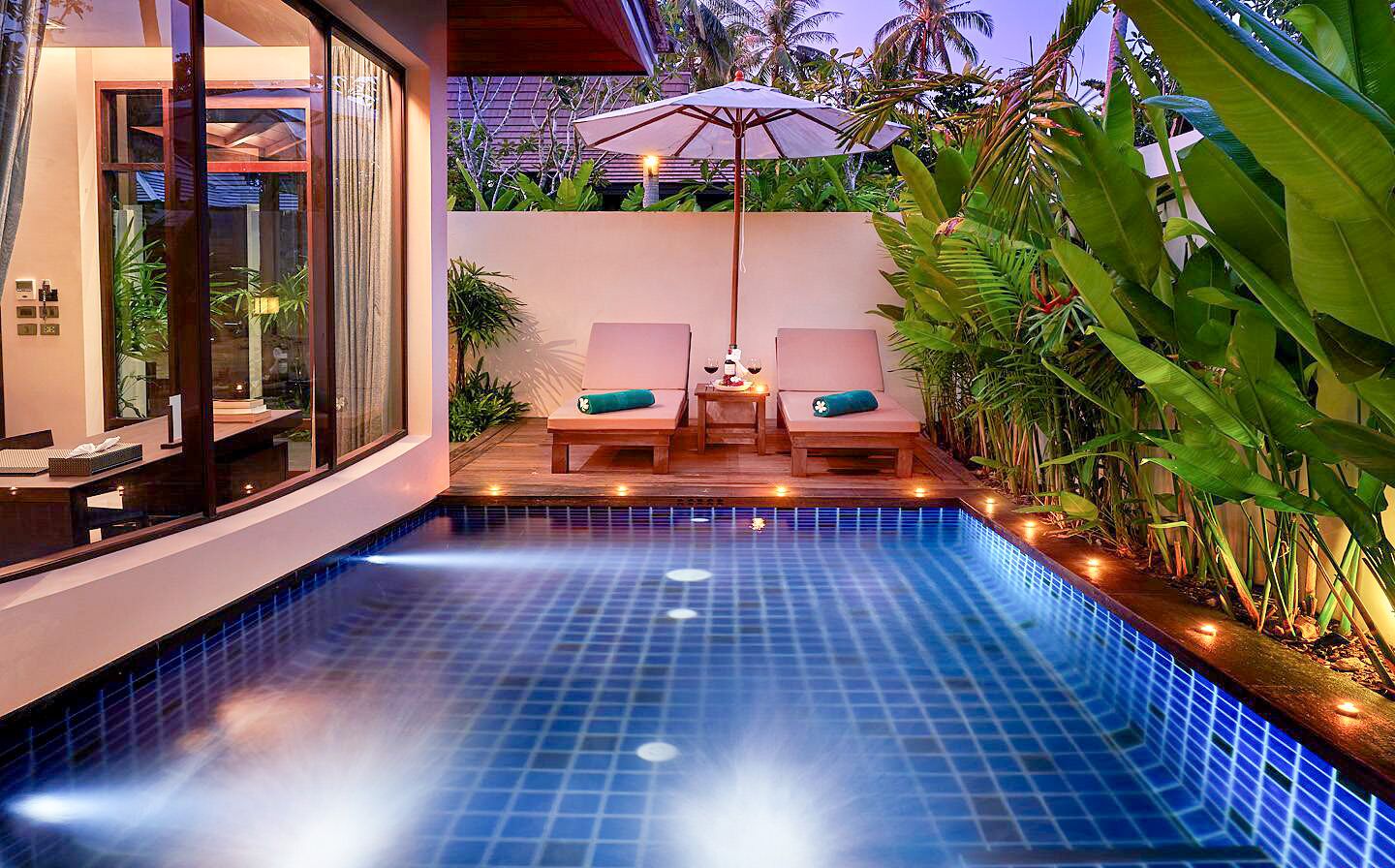 A swimming pool with two lounge chairs and an umbrella, surrounded by lush greenery.