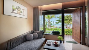 Una sala de estar moderna con sofá, una mesa de centro y vistas a una playa y follaje verde.