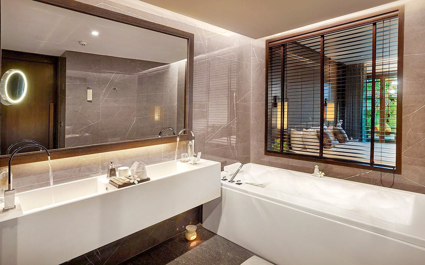 A modern bathroom with a large mirror, two sinks, a bathtub, and a window with blinds.