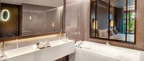 A modern bathroom with a large mirror, two sinks, a bathtub, and a window with blinds.
