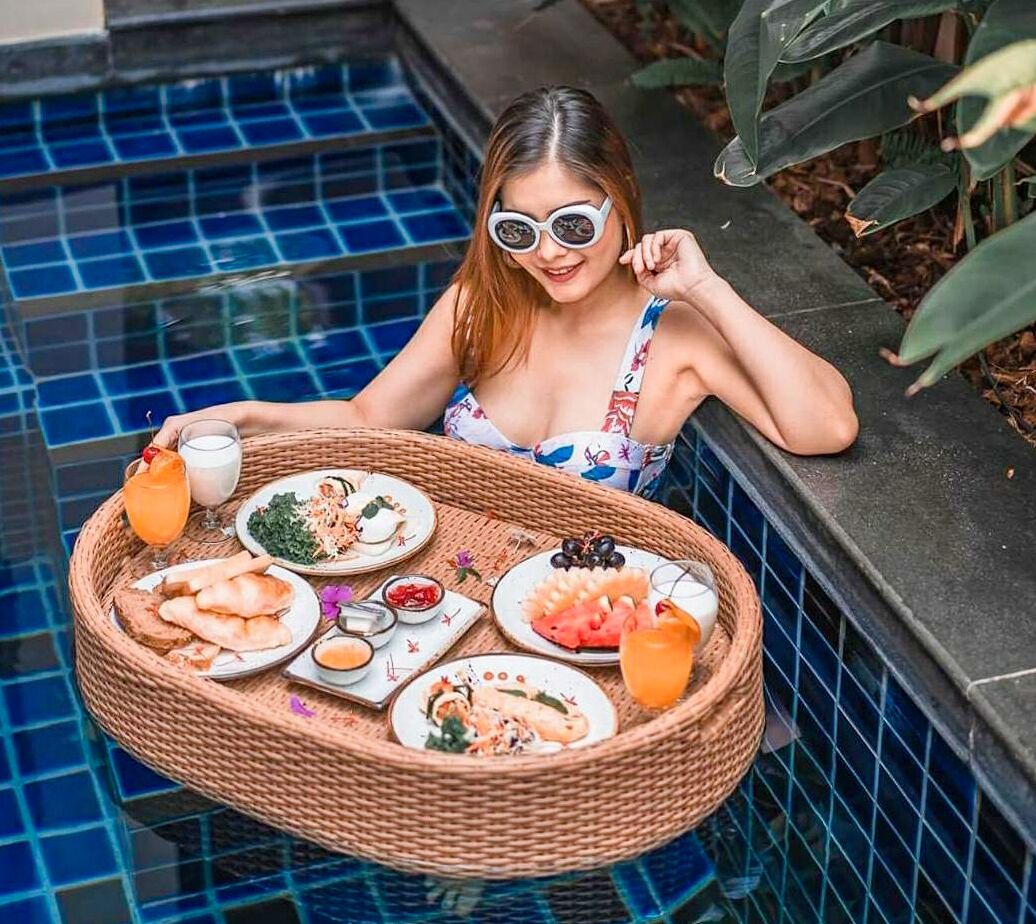 A person sitting by a pool with a tray of food and drinks.