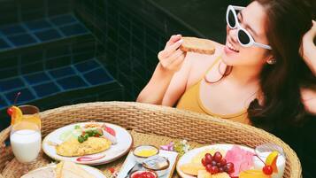 A wicker tray with a variety of breakfast items including toast, eggs, fruit, and a drink, placed on a tiled surface near a pool.