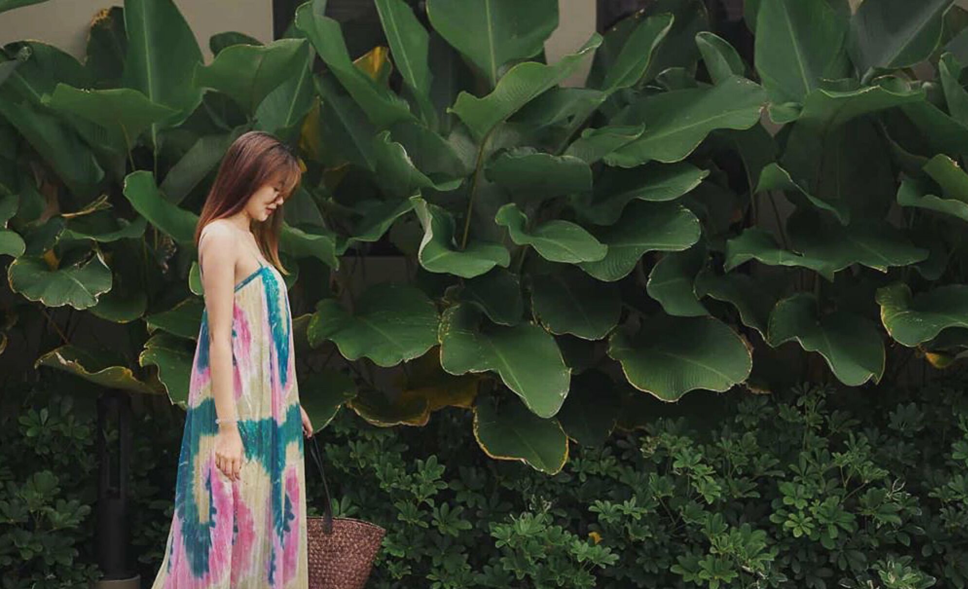 A woman in a colorful dress standing in a garden with large green leaves and small bushes.
