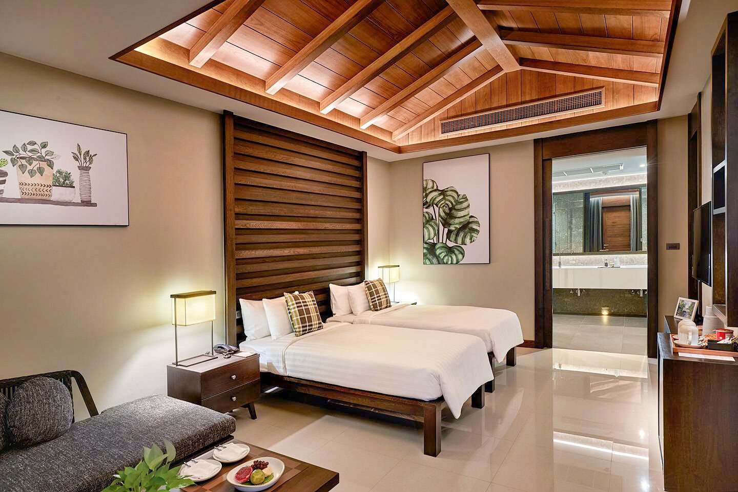Una habitación de hotel moderna con techo de madera, una cama grande, un sofá y un baño visible a través de una puerta abierta.