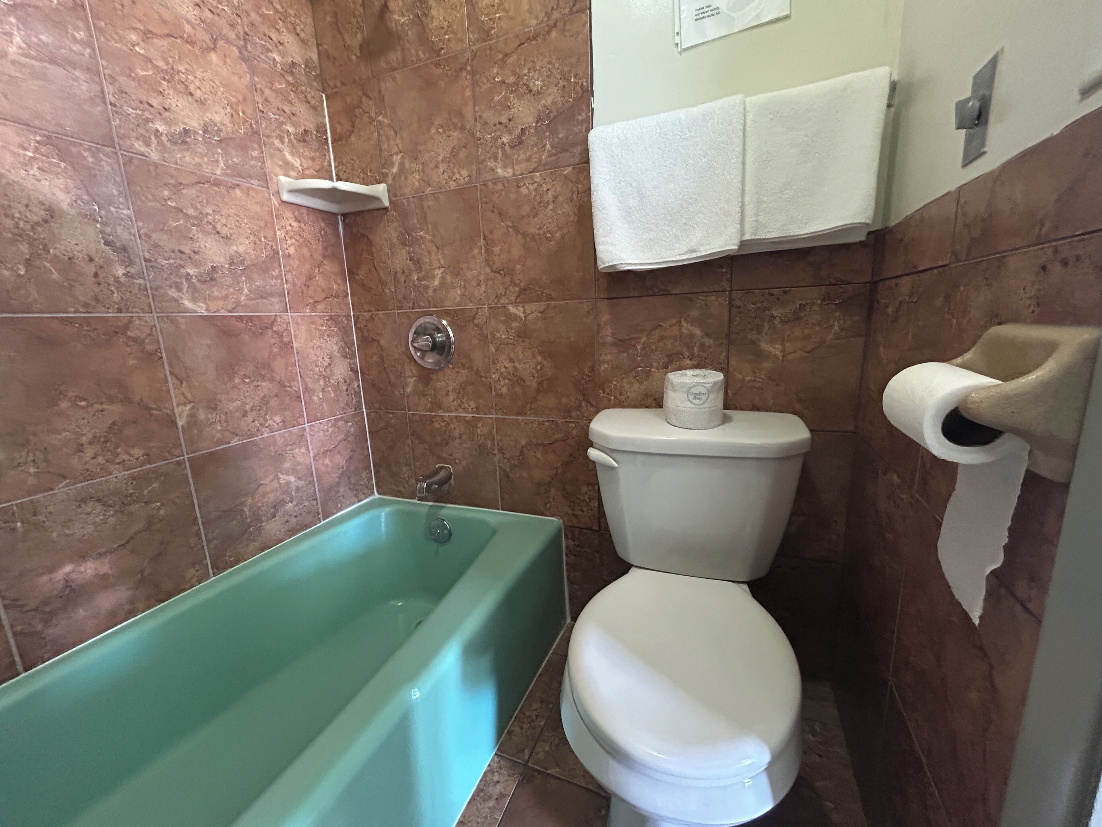 Casa de banho com banheira, sanita e suporte para toalhas de papel.