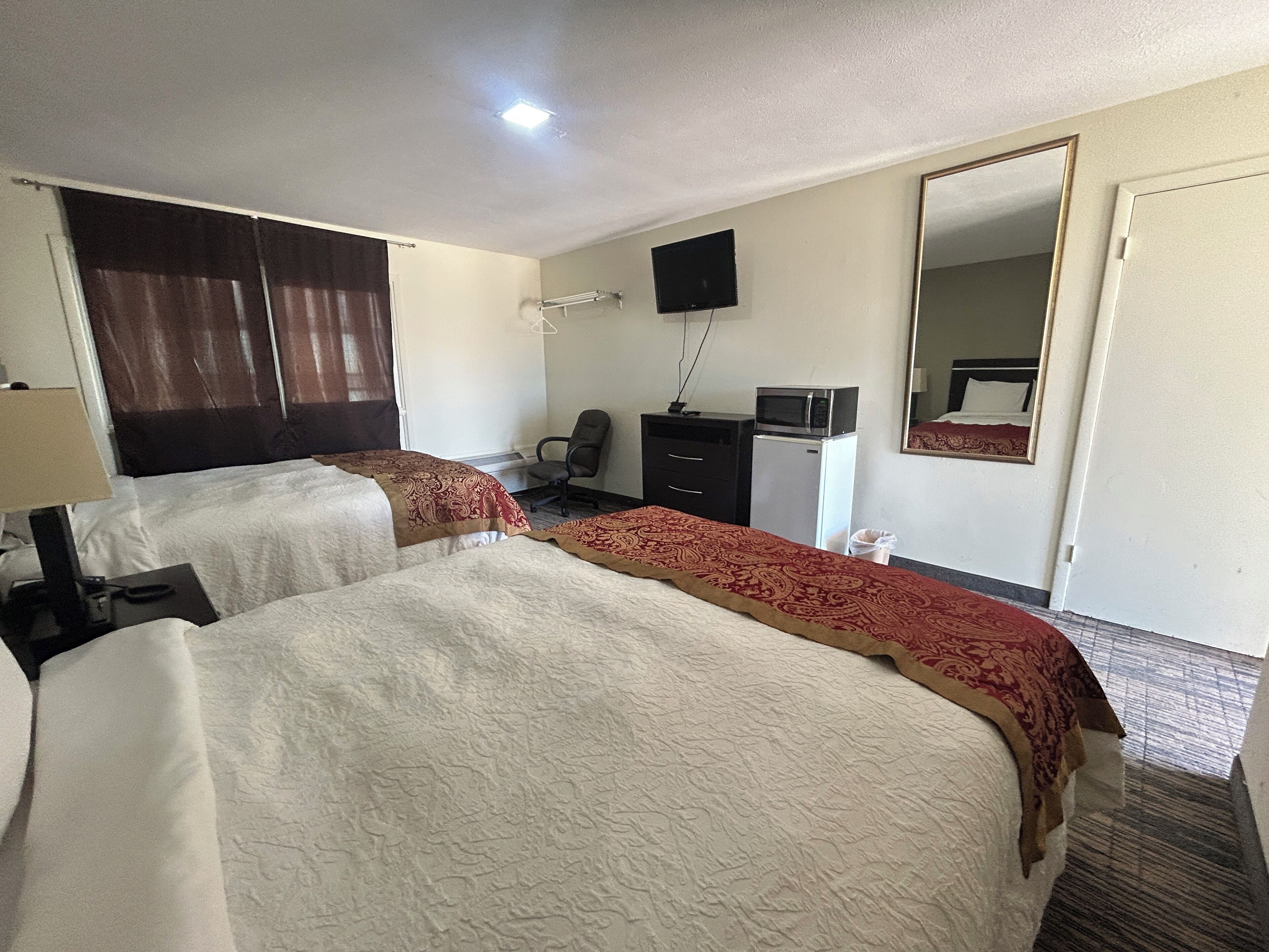 Une chambre d’hôtel avec deux lits, un bureau, une chaise, une télévision, une commode et un miroir.